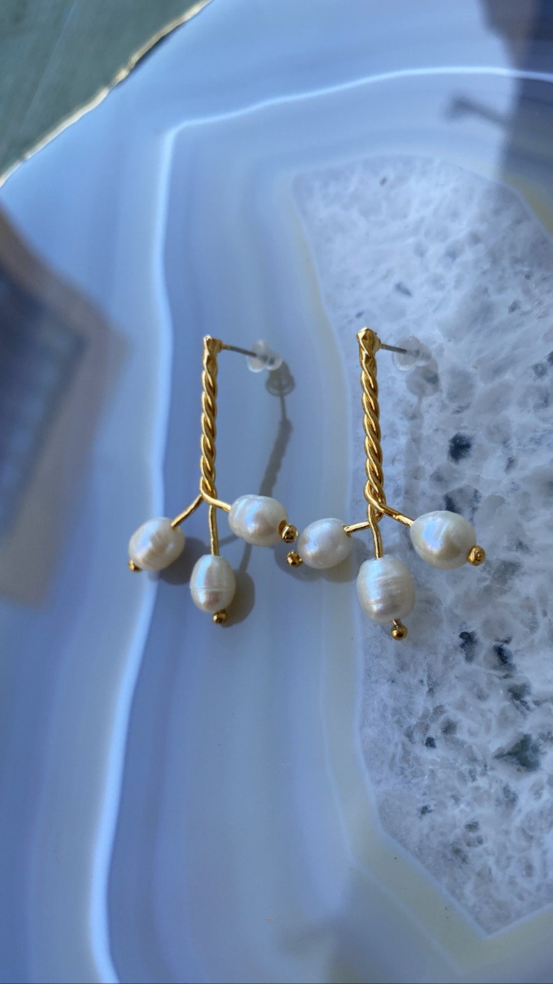 May include: A pair of gold earrings with a twisted wire design and multiple pearl drops.