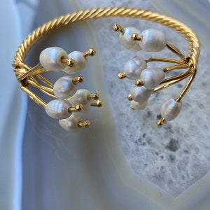 May include: A gold bangle bracelet with a twisted design and white pearl accents.