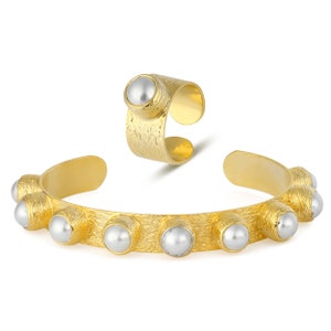 May include: A gold-toned bracelet and ring set with faux pearl accents. The bracelet has a textured finish and features a row of pearls around the band. The ring is also textured and has a single pearl on the top.