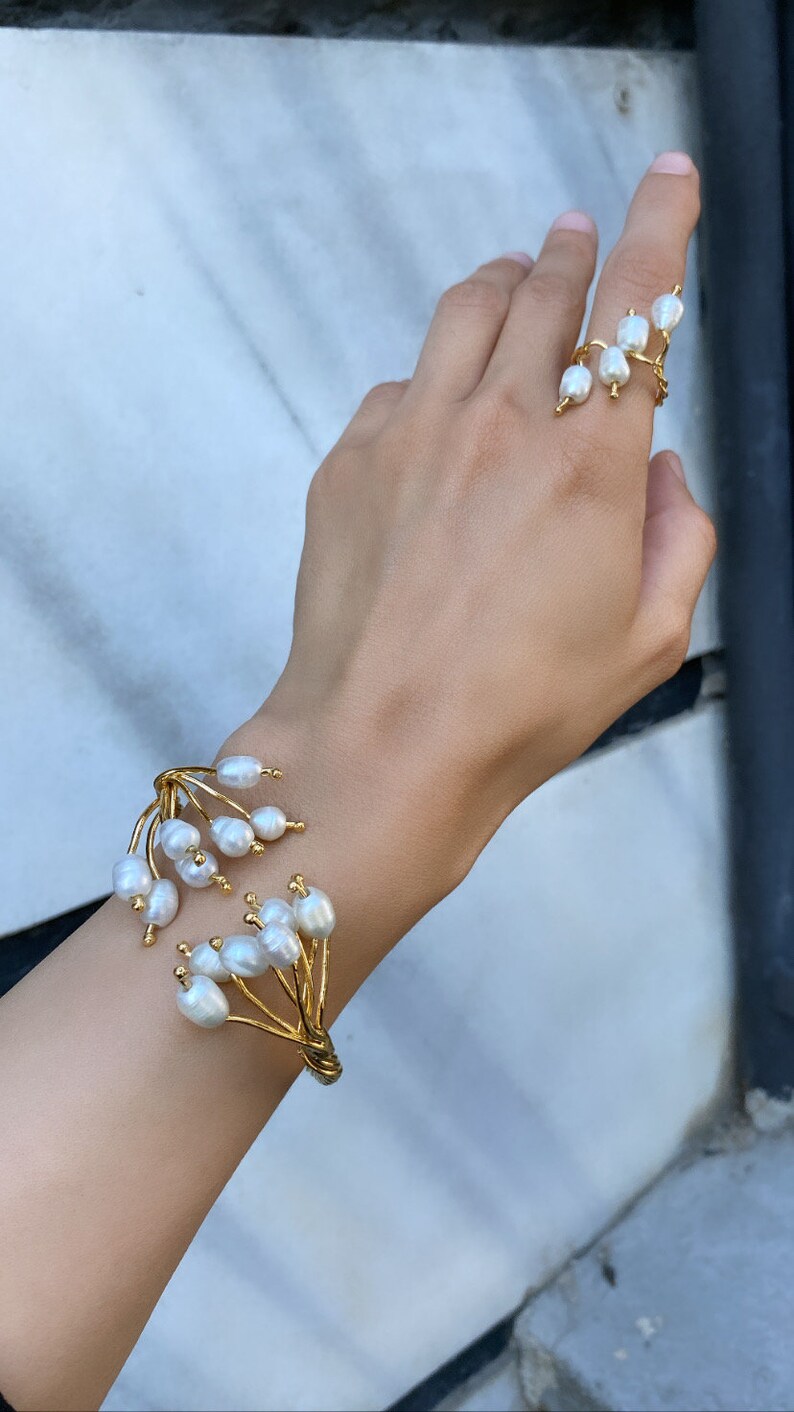 May include: A gold bracelet and ring set featuring white pearls. The bracelet has a delicate, branch-like design with multiple pearls clustered together. The ring features a single pearl on a thin band.