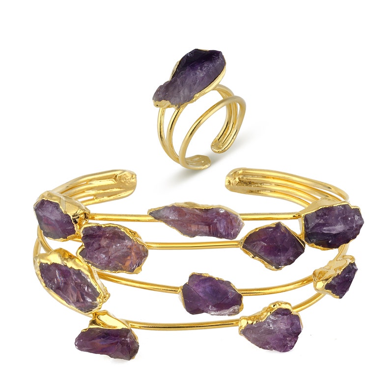 May include: A set of gold-toned bracelets with amethyst stones. The bracelets are stacked on top of each other and feature multiple amethyst stones of varying sizes. A matching ring with an amethyst stone is also included.
