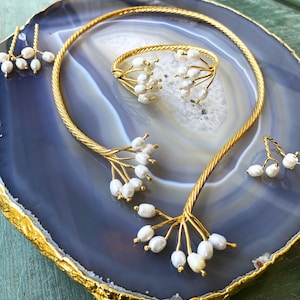 May include: A set of gold jewellery featuring a delicate necklace, a ring, and earrings. Each piece is adorned with small white pearls arranged in a branch-like pattern.