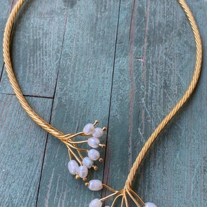 May include: A gold choker necklace with a twisted rope design and pearl accents. The pearls are clustered at the ends of the necklace, creating a delicate and feminine look.