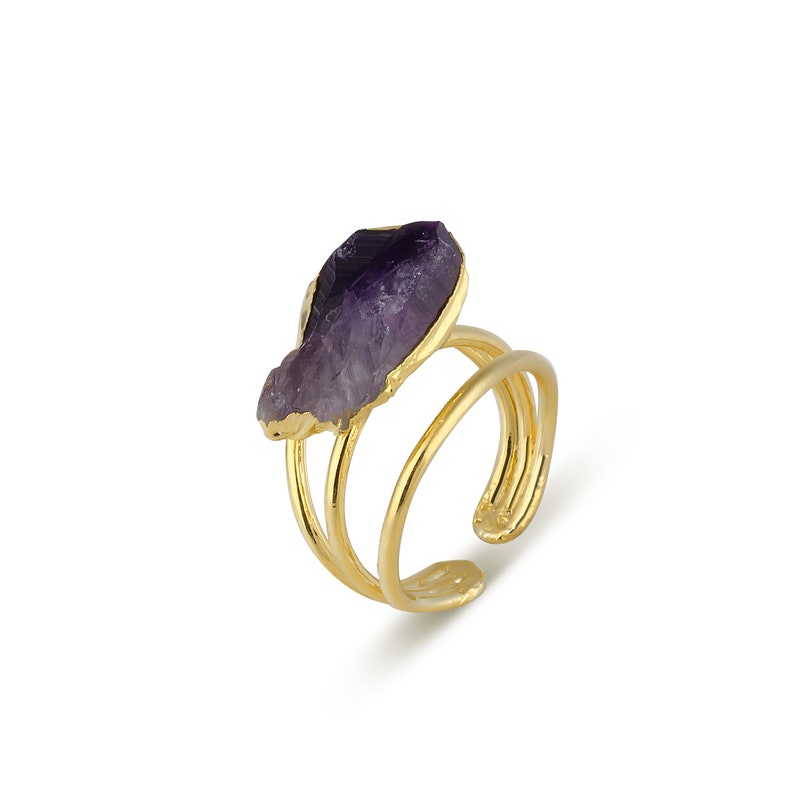 May include: A gold ring with a purple amethyst stone. The ring has a double band design.