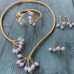 May include: A gold necklace, bracelet and earrings set with pearl accents. The jewellery features a delicate, branch-like design with small white pearls.