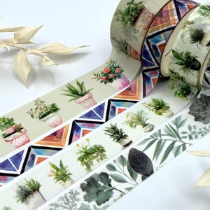 Könnte beinhalten: Vier Rollen Washi-Tape mit verschiedenen Designs. Die erste Rolle hat ein Aquarellmuster mit Pflanzen in Töpfen. Die zweite Rolle hat ein geometrisches Muster in den Farben Blau, Lila, Orange und Rosa. Die dritte Rolle hat ein Aquarellmuster mit Pflanzen in Töpfen. Die vierte Rolle hat ein Aquarellmuster mit Blättern.