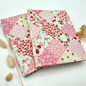 Könnte beinhalten: Zwei rechteckige Journale mit Patchwork-Einbänden. Die Einbände weisen eine Vielzahl von rosa Mustern auf, darunter Punkte, Erdbeeren und florale Designs. Die Journale sind mit Trockenblumen verziert.