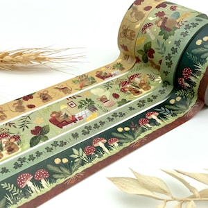 Könnte beinhalten: Drei Rollen dekoratives Washi-Tape mit Illustrationen von Mäusen in einem Wald. Die Designs zeigen Pilze, Blätter und Waldelemente in Grün, Braun und Rot. Ideal zum Scrapbooking und Basteln. Jede Rolle ist etwa 1,5 cm breit.
