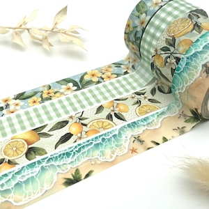 Könnte beinhalten: Dekorative Washi-Tape-Rollen mit verschiedenen Designs. Die Rollen zeigen Muster von Zitronen, Blumen und Strandszenen mit Meereswellen. Das Klebeband ist in Grün-, Gelb- und Blautönen gehalten, ideal für Bastelarbeiten und Scrapbooking.