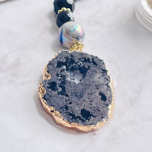 May include: A black agate pendant with a gold rim. The pendant is attached to a black and iridescent beaded necklace.