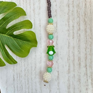 May include: A green frog charm with white eyes and a pink and green beaded phone charm.