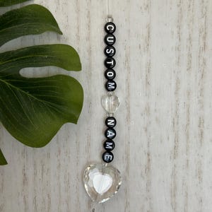 May include: A black beaded car charm with the words "CUSTOM NAME" and a clear crystal heart.