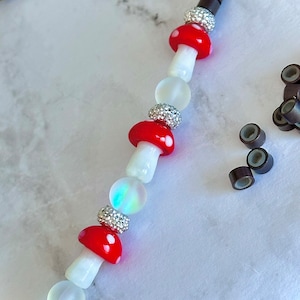 Puede incluir: Un collar de cuentas blancas y rojas con cuentas con forma de hongo y detalles plateados. El collar está sobre una superficie de mármol blanco.