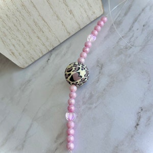May include: A pink beaded phone charm with a leopard print charm. The beads are iridescent and have a pearlescent finish.