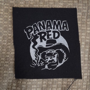 May include: Black fabric patch with a white embroidered design. The design features a cartoon character with a hat and the text "PANAMA RED".
