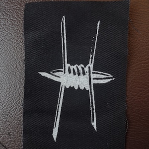 Puede incluir: Un parche de tela negro con un diseño de alambre de púas blanco.