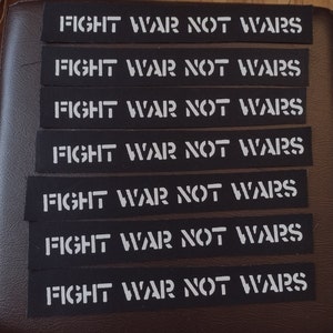 Może przedstawiać: Siedem czarnych naszywek z tkaniny z białym napisem "FIGHT WAR NOT WARS". Naszywki są prostokątne i ułożone w schludny stos. Tekst jest pogrubiony, bezszeryfowy.