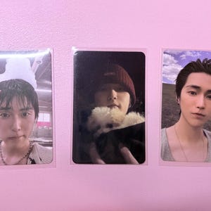 May include: Three photo cards featuring different individuals. The first card shows a person with dark hair, wearing a patterned sweater and necklace. The second card shows a person wearing a beanie and holding a small, fluffy dog. The third card shows a person in a tank top.