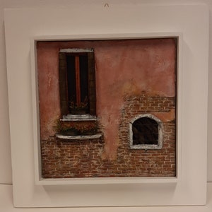 Könnte beinhalten: Ein gerahmtes Gemälde einer Backsteinmauer mit einem Fenster und einem kleinen Bogenfenster. Die Wand ist in Rosatönen und Braun gestrichen. Das Fenster hat einen Holzrahmen und ist mit Blumen verziert. Das Bogenfenster hat ein Metallgitter.