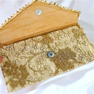 May include: A gold and cream embroidered clutch purse with a decorative clasp. The purse is open and the interior is visible.