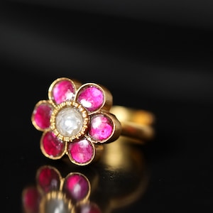 May include: A gold ring featuring a flower design. The flower has seven pink gemstones and a single white gemstone in the centre.