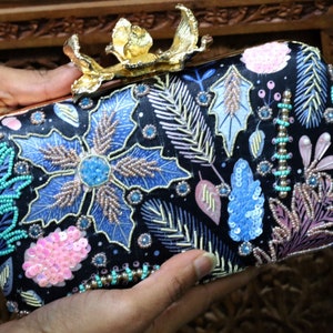 May include: A black clutch bag with a floral design embroidered with sequins and beads. The bag has a gold metal clasp in the shape of a flower.