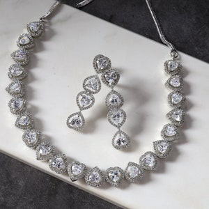 Pode incluir: Um conjunto de colar e brincos de prata com um design em forma de lágrima. As joias são adornadas com pedras de zircônia cúbica transparentes.