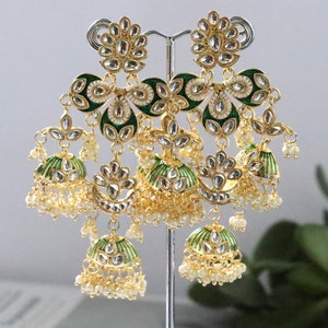 Pode incluir: Um par de brincos de ouro com detalhes em esmalte verde e branco e pérolas. Os brincos são pendentes e têm um design de vários níveis.