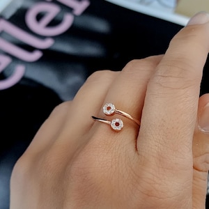 May include: A rose gold ring with two round clear stones set in a circle design. The ring is open and wraps around the finger.