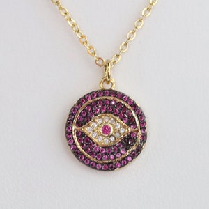May include: Gold chain necklace with a round pendant featuring a pink and white evil eye design.