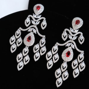 Puede incluir: Un par de pendientes de plata con detalles de cristal rojo. Los pendientes tienen un diseño delicado de hojas con múltiples niveles de pequeños cristales.