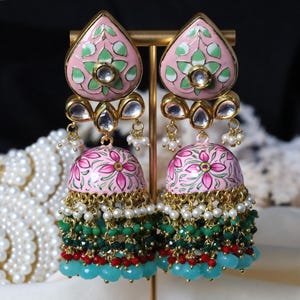 Pode incluir: Um par de brincos rosa e dourado com desenhos florais, contas verdes e azuis e pérolas brancas.