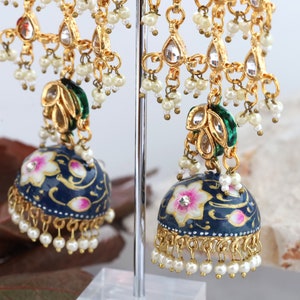 May include: A pair of blue and gold earrings with white pearl accents. The earrings feature a floral design and a green and gold pendant.