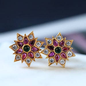 May include: A pair of gold earrings with a starburst design. The earrings are adorned with pink and green gemstones.