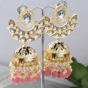 Pode incluir: Brincos de ouro com uma pedra grande, redonda e transparente cercada por pedras menores. Os brincos têm uma seção pendente com uma cúpula de esmalte azul e branco, pérolas brancas e contas cor-de-rosa.