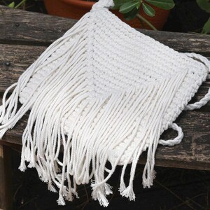 May include: White crocheted bag with long fringe. The bag has a simple design and is made of natural fibres.