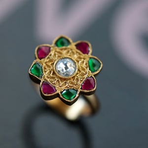 May include: A gold ring featuring a white gemstone surrounded by red and green gemstones.