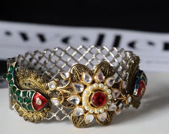 Könnte beinhalten: Ein silbernes und goldenes Armreif-Armband mit einem floralen Design und zwei Fischmotiven. Das Armband ist mit roten, grünen, blauen und weißen Edelsteinen verziert.