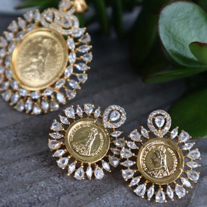 May include: A gold pendant and earrings set with a coin design. The pendant and earrings are surrounded by clear, sparkling stones.