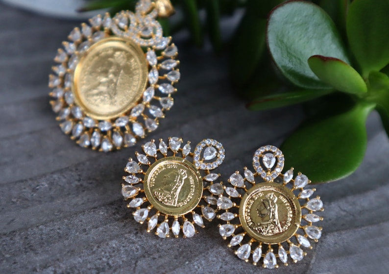 May include: A gold pendant and earrings set with a coin design. The pendant and earrings are surrounded by clear, sparkling stones.
