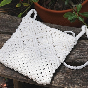 May include: White crocheted bag with a long strap. The bag has a square pattern and is made of a thick, textured yarn.