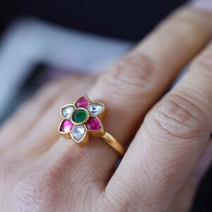 May include: A gold ring with a flower design featuring pink, white and green gemstones.