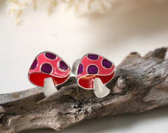 May include: A pair of silver mushroom stud earrings with pink and purple enamel. The mushrooms have white stems and purple polka dots.