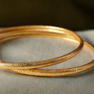 Puede incluir: Dos brazaletes de oro con un diseño texturizado y estampado. Los brazaletes están apilados uno encima del otro.
