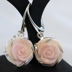 May include: A pair of silver dangle earrings with pink rose-shaped carved shell pendants.