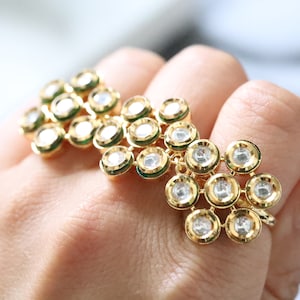 Puede incluir: Un anillo de oro con múltiples capas de piedras redondas transparentes engastadas en oro con acentos verdes.