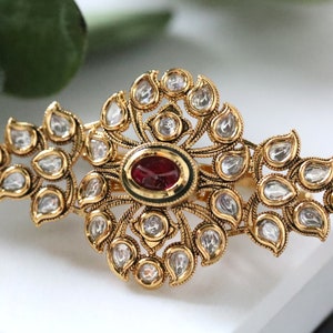 Puede incluir: Un anillo de oro con una piedra roja en el centro y un diseño de pequeñas piedras blancas alrededor.