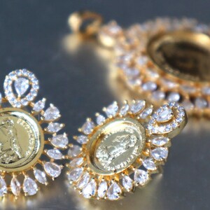 May include: A set of gold-tone earrings and a pendant necklace featuring a coin design with a profile of a woman. Each piece is adorned with clear cubic zirconia stones.
