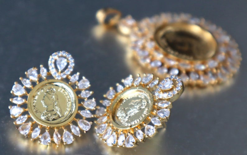 May include: A set of gold-tone earrings and a pendant necklace featuring a coin design with a profile of a woman. Each piece is adorned with clear cubic zirconia stones.