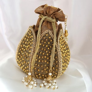 May include: A gold beaded clutch bag with a brown fabric lining and a drawstring closure. The bag is shaped like a lotus flower and has pearl embellishments.